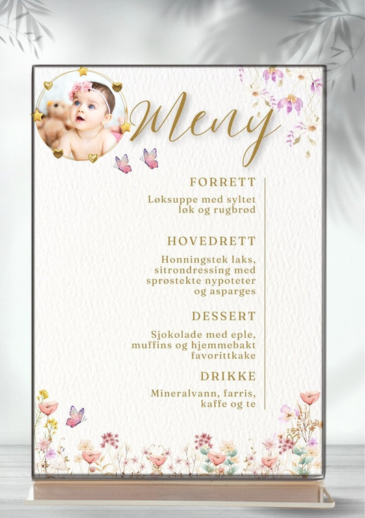 Meny til dåp eller navnefest i akrylramme med babybilde i sirkelramme med gullhjerter og stjerner. Rosa og lilla blomster og sommerfugler. Meny viser forrett, hovedrett, dessert og drikke.