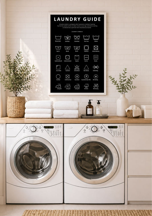 Vaskeromsskilt med Laundry Guide i sort ramme over vaskemaskin og tørketrommel – plakat med vaskesymboler og instruksjoner for klesvask, i sort og hvit fargepalett, i moderne vaskerom med hvite fliser og trebenk 